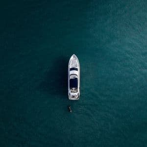 Veduta aerea dall'alto di uno yacht bianco e di un'imbarcazione più piccola che galleggiano su acque calme, blu-verdi scure.