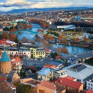 Vue aérienne d'une ville traversée par une rivière, présentant un mélange de toits historiques colorés et d'architecture moderne.