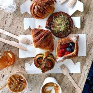 Una veduta dall'alto di pasticcini assortiti, un caffè freddo e un latte macchiato con latte art, disposti su un tavolo di marmo.