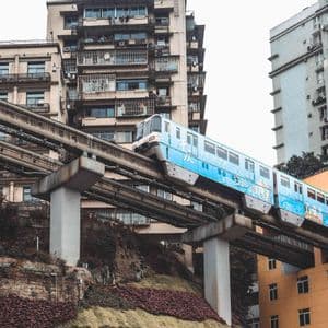Un treno monorotaia blu su un binario sopraelevato attraversa un'apertura in un edificio residenziale in una zona urbana densa.