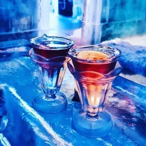Due bicchierini da shot di ghiaccio, pieni di una bevanda rossa, sono su un bancone del bar anch'esso di ghiaccio con illuminazione blu.