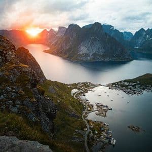 Veduta panoramica di un fiordo e di un borgo costiero incastonato tra ripide montagne al tramonto vibrante.