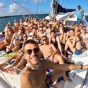 Un numeroso gruppo WeRoad sorride e posa per un selfie sul ponte di un catamarano che naviga in mare aperto.