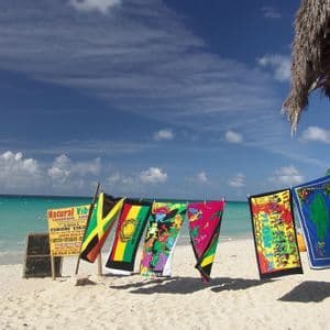 Asciugamani e bandiere souvenir colorati sono appesi a uno stendibiancheria su una spiaggia sabbiosa accanto all'oceano turchese sotto un cielo blu.
