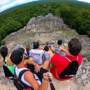 Un groupe WeRoad prend un selfie assis au sommet d'anciennes ruines de pierre, surplombant une vaste jungle verdoyante.