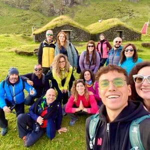 Eine WeRoad-Gruppenreise lächelt für ein Selfie auf einem grasbewachsenen Feld vor Steinhäusern mit Torfdächern.