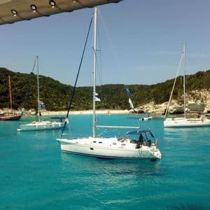Veleros anclados en una bahía tranquila con agua turquesa, una playa de arena y colinas verdes cubiertas de árboles.
