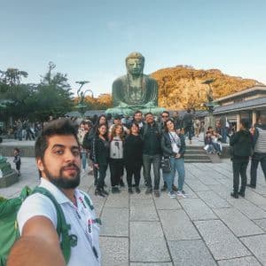 Un hombre se toma una selfie con un grupo de viaje de WeRoad posando en un patio frente a una gran estatua de bronce de Buda.