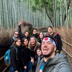 Un gruppo WeRoad scatta un selfie sorridente su un sentiero all'interno di una fitta foresta di bambù.