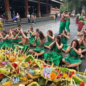 Un groupe WeRoad en tenue de cérémonie verte est assis au sol, priant devant des offrandes florales colorées.