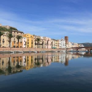 Edifici colorati sul lungomare e palme si riflettono nell'acqua calma di un fiume sotto un cielo azzurro e limpido.