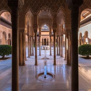 Una vista simétrica de un patio ornamentado con esbeltas columnas, arcos detallados y una fuente central en un suelo de mármol.