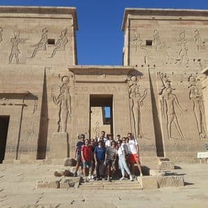 Un grupo de WeRoad posa para una foto en las escaleras de un gran templo egipcio antiguo con tallas jeroglíficas bajo un cielo azul claro.