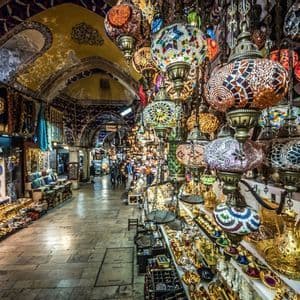 Colorful mosaic lamps hang for sale in a bustling indoor market with arched ceilings and stalls filled with goods.