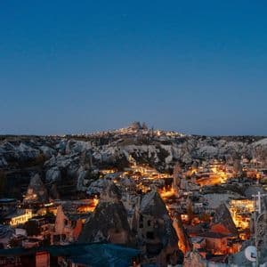 Une ville nichée parmi des formations rocheuses uniques, illuminée par les lumières au crépuscule sous un ciel bleu clair.