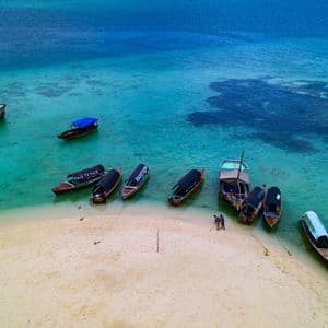 Luftaufnahme von Holzbooten, die auf einer Sandbank festgemacht sind, umgeben von türkisfarbenem und tiefblauem Tropenwasser.
