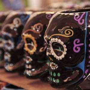 Primo piano di tazze a teschio Calavera in ceramica nera con disegni colorati dipinti a mano, allineate in fila.