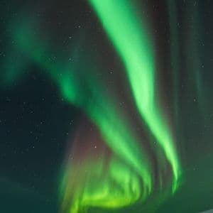 Lebhaft grüne Nordlichter wirbeln am sternenklaren Nachthimmel über einer schneebedeckten Berglandschaft.
