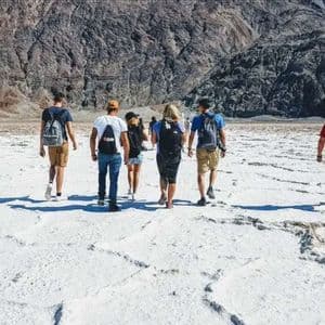 A WeRoad group trip walks across a vast, white salt flat with a rocky mountain range in the background.