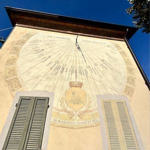Inquadratura dal basso di una grande meridiana decorata, dipinta sulla facciata di un edificio sotto un cielo azzurro e limpido.