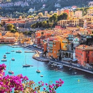 Edifici colorati si raggruppano su una collina attorno a una luminosa baia turchese, piena di barche a vela e yacht.