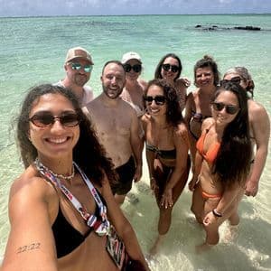 Un groupe WeRoad en voyage prend un selfie collectif dans une eau de mer claire et peu profonde sous un ciel lumineux.