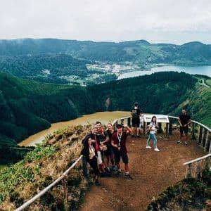 Un groupe WeRoad pose pour une photo depuis un point de vue surplombant un vaste paysage de collines verdoyantes et deux lacs aux couleurs différentes.