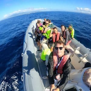 A WeRoad group trip smiling for a selfie on a rigid inflatable boat sailing on the open blue sea.