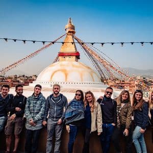 Eine WeRoad-Gruppe posiert gemeinsam auf einem Dach mit einer großen weißen Stupa und Gebetsfahnen im Hintergrund.