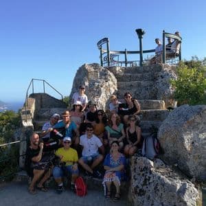 Eine WeRoad-Gruppe posiert für ein Foto auf Steinstufen an einem Aussichtspunkt mit Blick auf Meer und Küste.