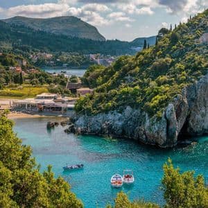 Barche galleggiano su acqua turchese in una baia circondata da rigogliose scogliere verdi e un piccolo villaggio sulla spiaggia.