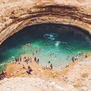 Una vista aérea de muchas personas nadando y relajándose en el agua turquesa de un gran cenote rodeado de acantilados rocosos.
