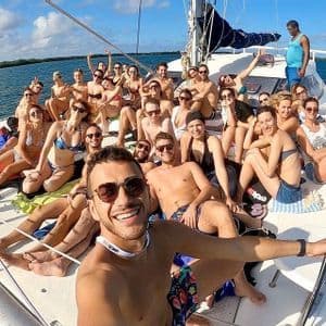 Eine WeRoad-Gruppe lächelt und posiert für ein Selfie an Deck eines Katamarans, der auf dem Meer segelt.