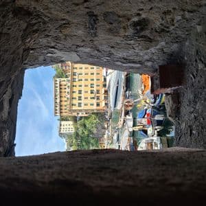 A harbor with colorful buildings and boats is seen through a rectangular opening in a rough stone wall.