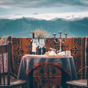 Una mesa para dos con vino y queso, con vistas a una vasta cordillera bajo un cielo nublado.