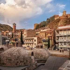 Una vista sobre cúpulas de ladrillo hacia coloridos edificios de la ciudad, anidados al pie de una gran colina coronada por una fortaleza.
