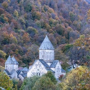 Un monasterio de piedra con chapiteles cónicos está rodeado por un denso bosque en la ladera en pleno color otoñal.