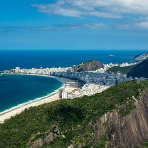 Une vue aérienne d'une ville côtière le long d'une plage de sable incurvée, nichée entre des montagnes verdoyantes et l'océan bleu.