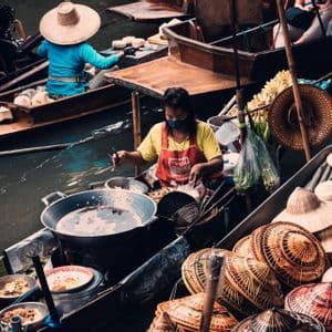 Una vista aerea di un mercato galleggiante con venditori su barche che cucinano cibo e vendono cappelli di paglia.