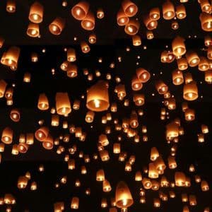 Centinaia di lanterne di carta illuminate fluttuano nel cielo notturno, brillando caldamente.