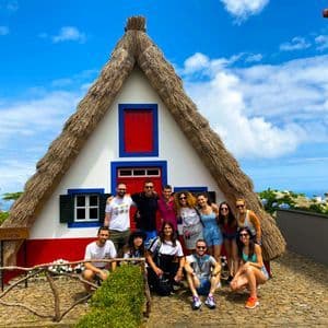 Un gruppo WeRoad in viaggio posa per una foto davanti a una tradizionale casa con tetto di paglia a capanna in una giornata di sole.