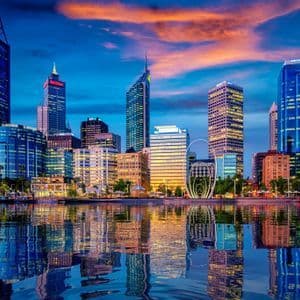 Uno skyline moderno con grattacieli illuminati si riflette nell'acqua sottostante al tramonto.