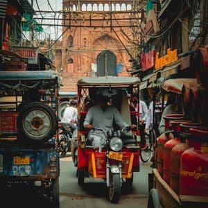 Un tuk-tuk circula por una calle estrecha y concurrida con cables aéreos enredados, con un gran edificio histórico de fondo.