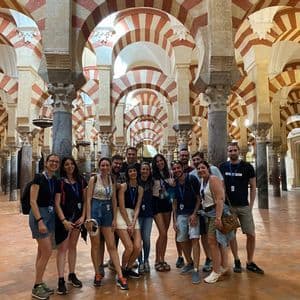 Un viaggio di gruppo WeRoad in posa per una foto all'interno di una grande sala con archi a strisce rosse e bianche e numerose colonne.