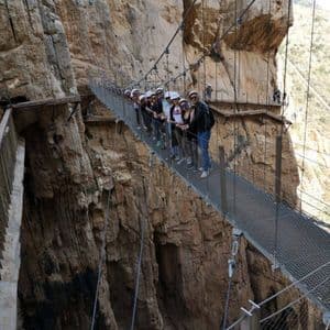 Eine WeRoad-Reisegruppe mit Helmen posiert für ein Foto auf einer Hängebrücke, die an einer steilen Canyonwand befestigt ist.