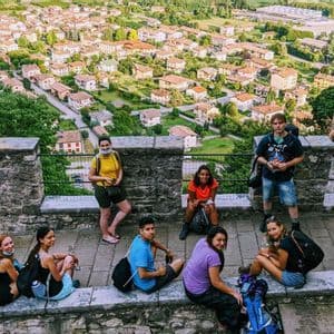 A WeRoad group trip of nine people posing on a stone terrace, with a town in a green valley visible in the background.