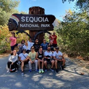 Eine WeRoad-Gruppenreise posiert für ein Foto am großen hölzernen Eingangsschild des Sequoia-Nationalparks.