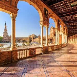 Un porticato curvo e coperto con archi in mattoni e colonne in pietra si affaccia su una grande piazza soleggiata con un edificio storico.