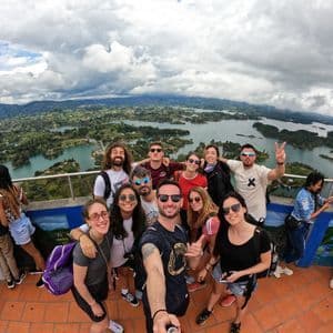 Eine WeRoad-Gruppe macht ein Gruppenselfie von einem Aussichtspunkt über einer weiten Landschaft aus Seen und grünen Hügeln.