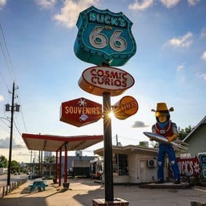 Panneaux routiers vintage pour la Route 66, souvenirs et jouets, avec une grande statue de cow-boy de l'espace devant un bâtiment.